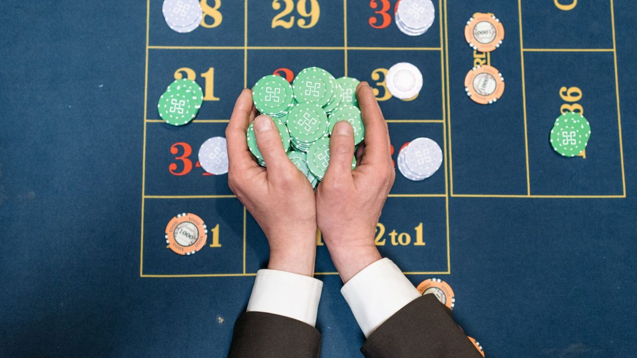 Hands in a suit holding poker chips on a casino gaming table.